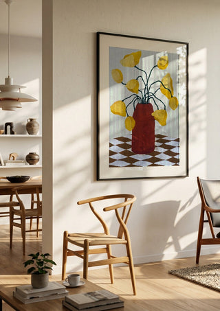 Gula blomster i terracottafärgad vas by Rebecka Hansson in a black frame in a bright dining room with wooden chairs
