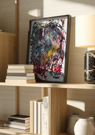 Tangle by Ronald Rumell in a dark frame on a wooden shelf beside books and a lamp