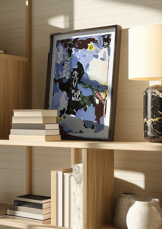 LOVE IS A DOG FROM HELL by Oscar Birch in a dark frame on a wooden shelf beside books and a lamp