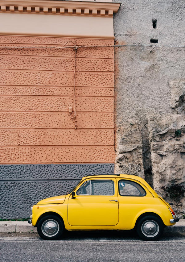 A yellow vintage car parked beside a textured wall on the Amalfi Coast Drive XII.