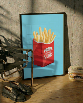 Poster featuring fries in a red carton with "Fries Before Guys" text, leaning against a wall.