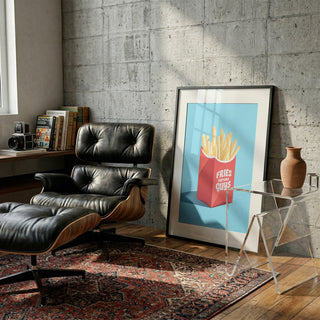 Fries Before Guys - Andreas Magnusson art print leaning on wall next to lounge chair in modern living room.