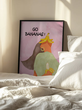 Framed "Go Bananas Playful" by Sannel Larson leaning on a bedroom wall beside a sunlit bed.