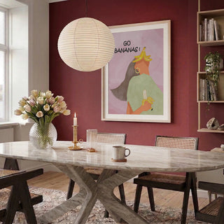 Go Bananas Playful by Sannel Larson framed on a red wall above a dining table with flowers and candles.