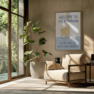Framed "Funny Bathroom Cat Welcome" poster by Andreas Magnusson displayed in a cozy, sunlit living space.