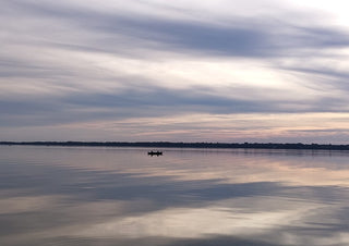Dusk Reflections by Bora Kőhalmi - banded dusk clouds mirrored in the still water of Lake Balaton with a small boat on the horizon