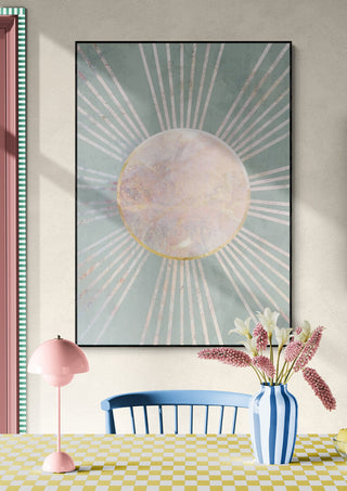 Sage green boho sun rays art print on wall above table with pink lamp, blue chair, and striped vase with flowers.