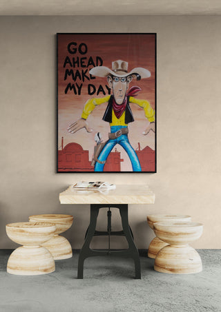 Wall art titled "Go Ahead - Daniel Leo" featuring a cartoon cowboy, displayed above a modern table and stools.