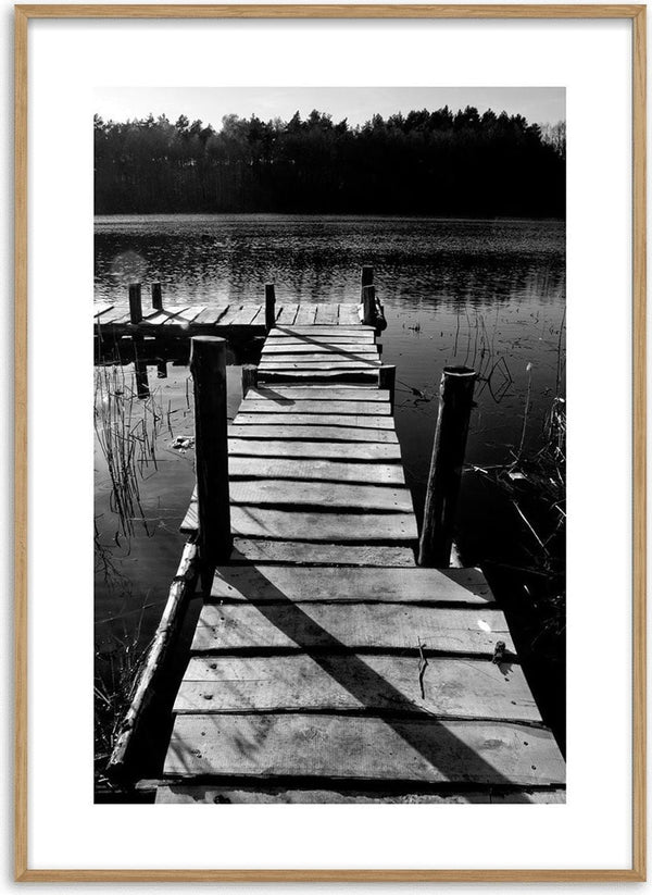 Black and white photo of a wooden jetty extending over a calm lake with trees in the background.