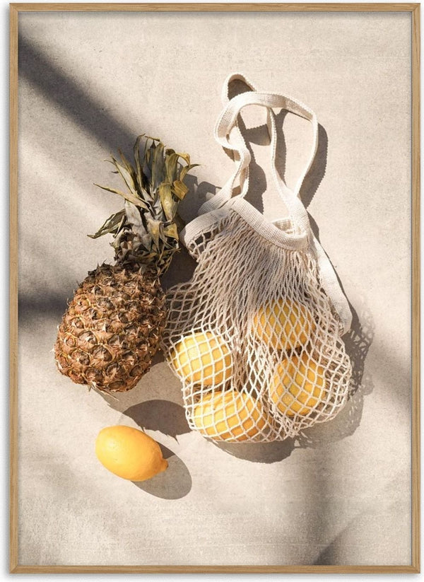 A pineapple and several yellow summer fruits in a mesh bag on a light surface.